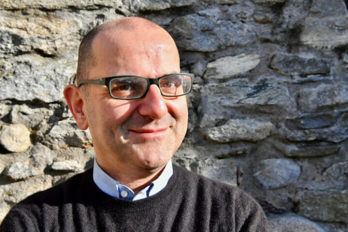 Ritratto di Alberto Pellai con occhiali, davanti a un muro in pietra, foto di repertorio