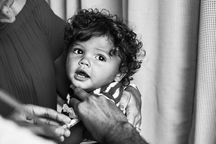 Bambino in braccio a un adulto durante una vaccinazione, foto di repertorio